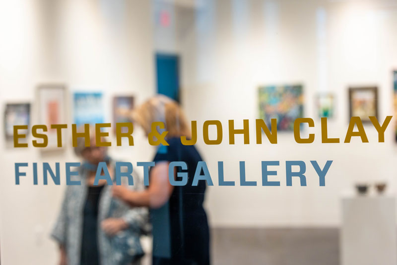 The sign for the Esther and John Clay Fine Arts Gallery on the glass outside the gallery.