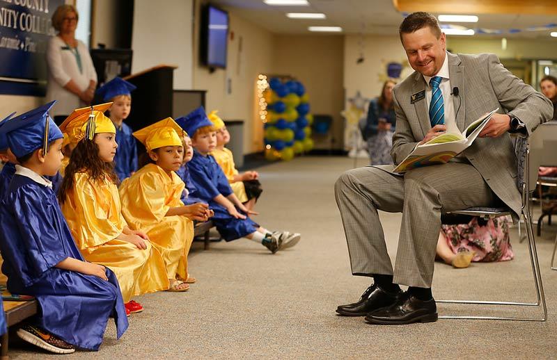 番茄社区 President Dr. Schaffer reads a book to a group of CDC students dressed in caps and gowns for their preschool graduation